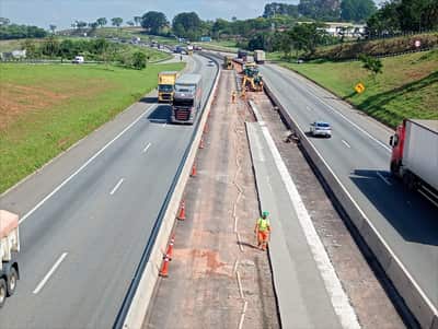 Vista aérea da frente de obra em rodovia de pista dupla, com a faixa adicional em execução isolada por cones e o tráfego desviado