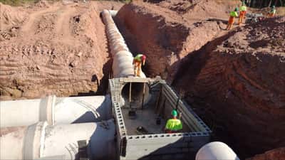 Assentamento de galeria de drenagem de grande diâmetro em vala escorada, com equipe de obra sobre o talude
